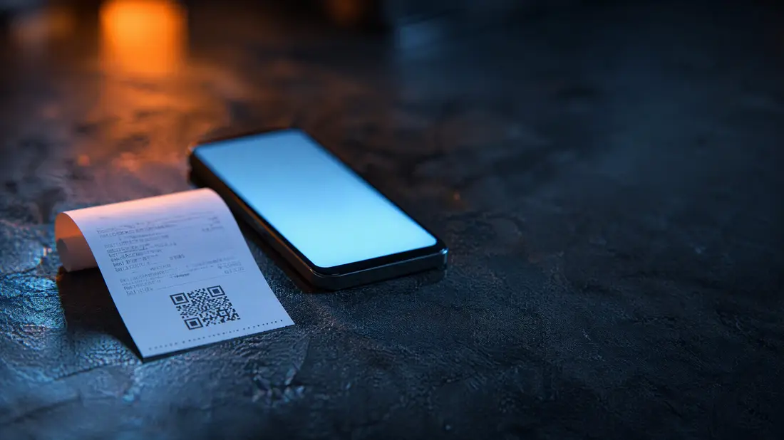 A receipt with a QR code beside a phone on a shop counter