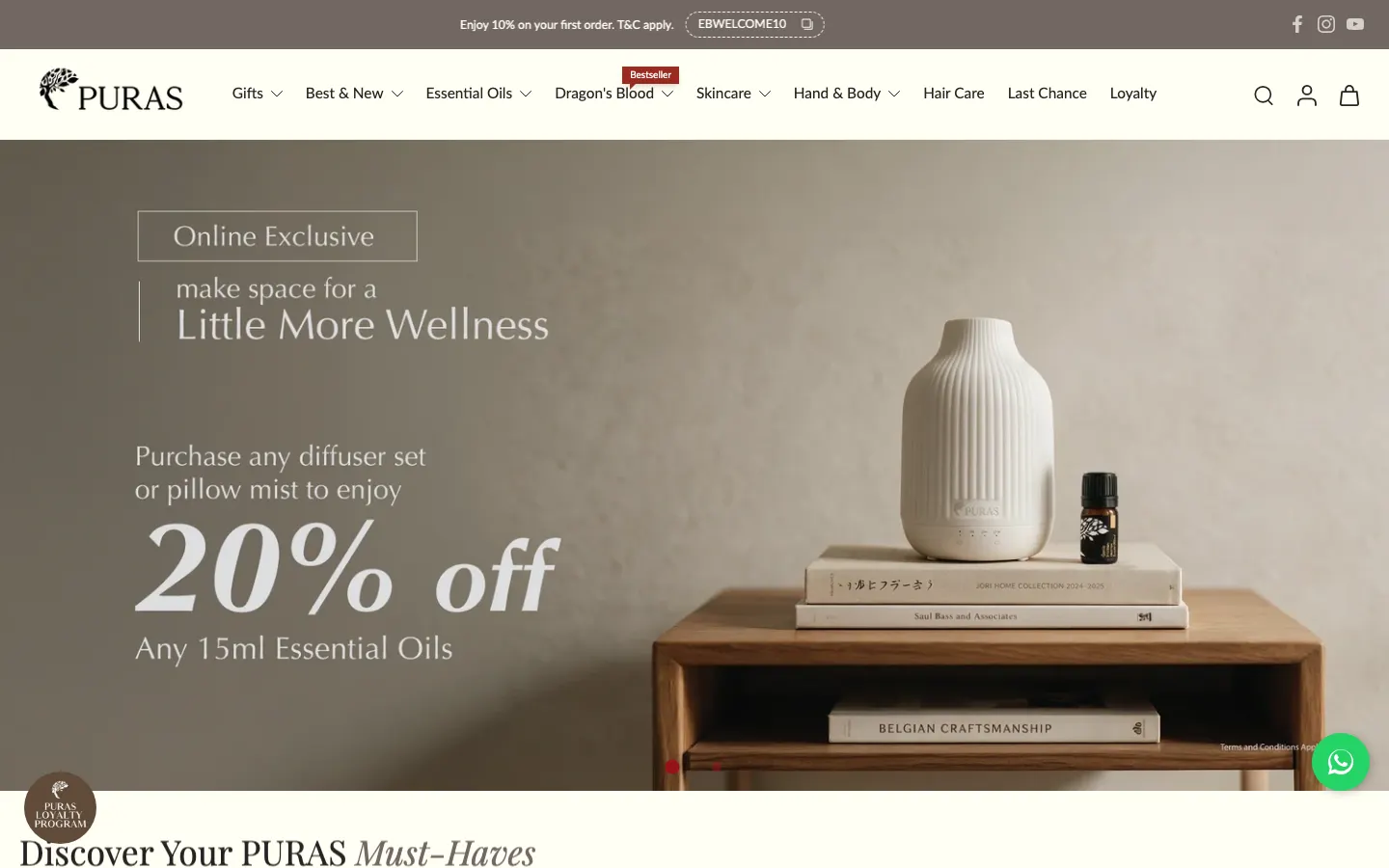 Puras homepage on desktop: diffuser on a wooden side table, a menu with Gifts, Essential Oils, Dragon's Blood and Loyalty, and a welcome code in the announcement bar